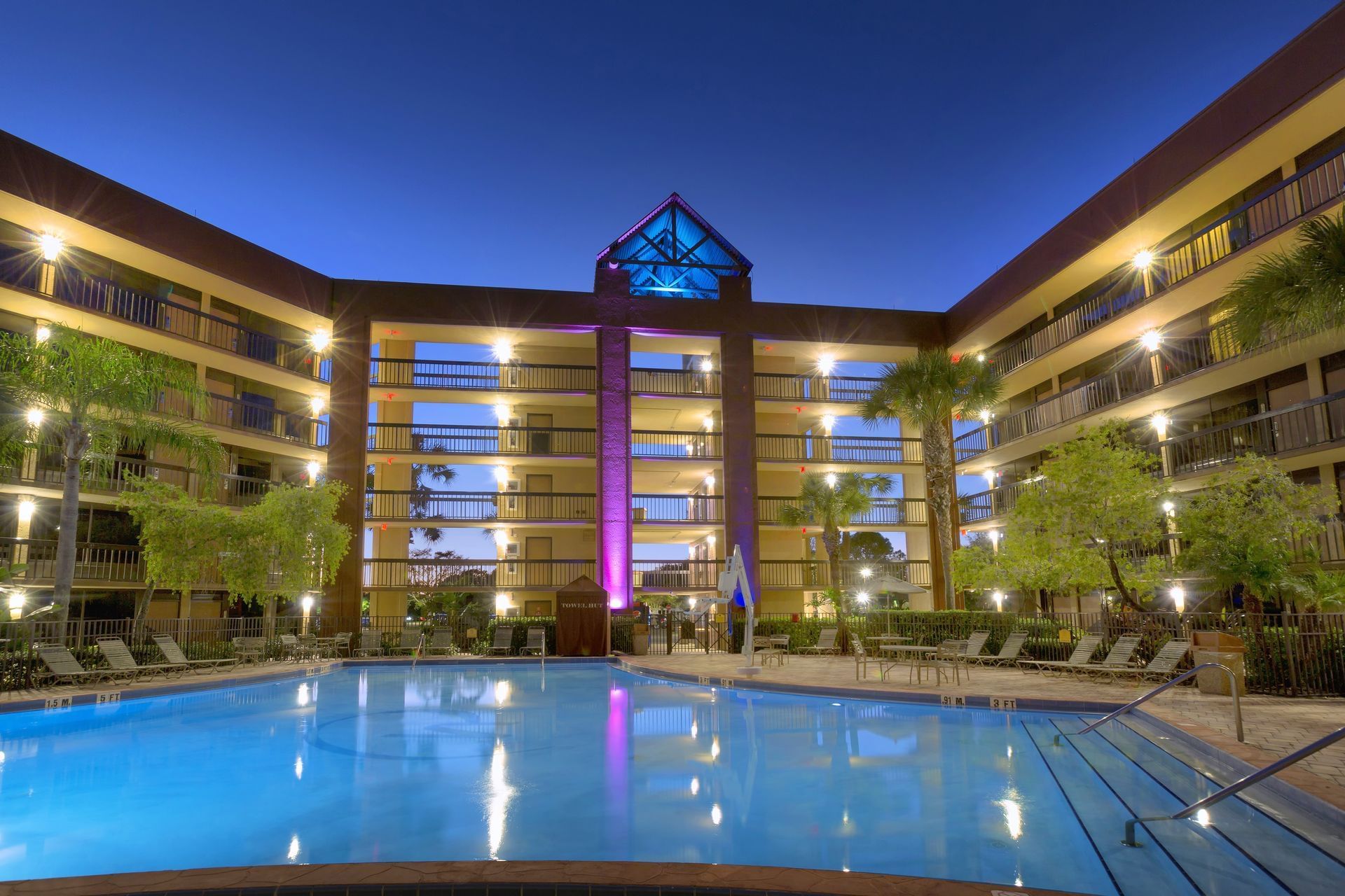 A beautiful hotel lit at night surrounding a blue pool at twilight. Stay at a Rosen Inn hotel when you attend family-friendly festivals in Orlando.