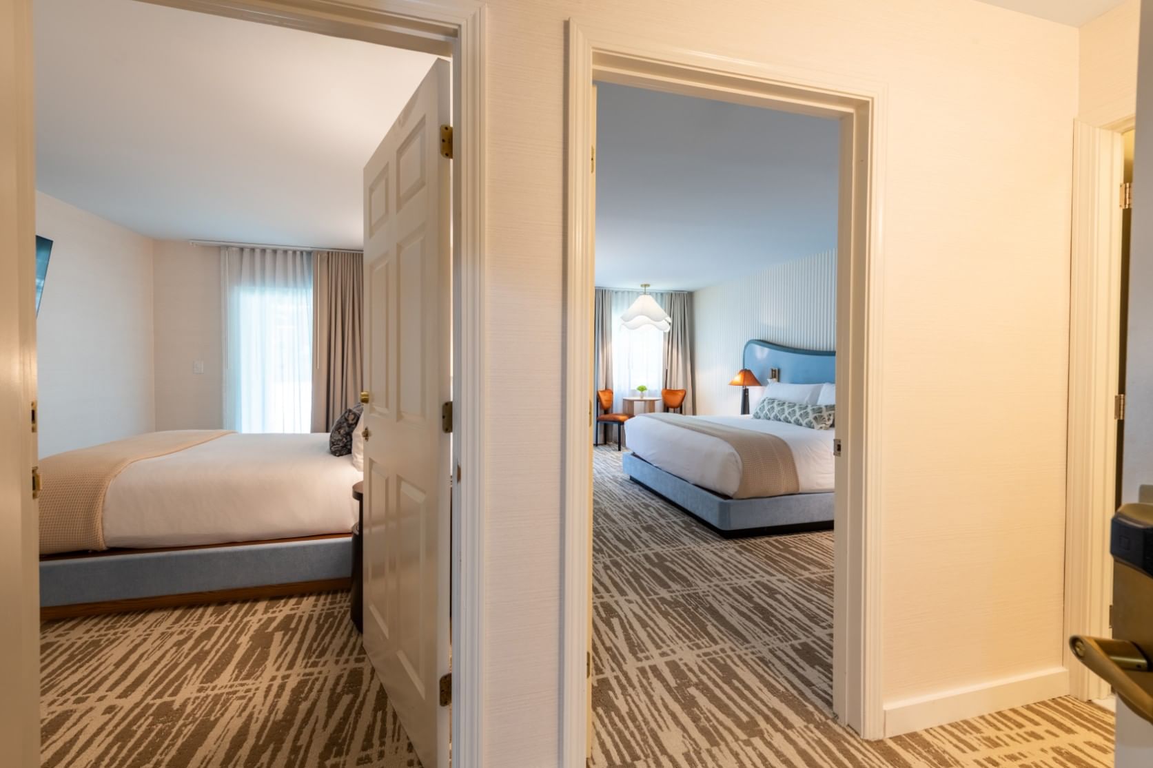 A hotel room with two beds, a carpeted floor, and a doorway leading to another area.