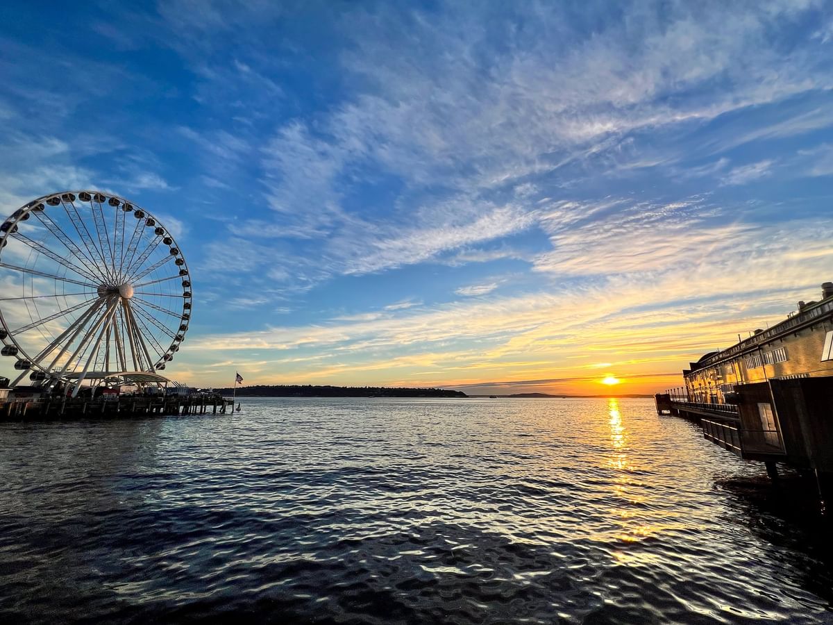 Large Ferris wheel by a wooden pier under a vibrant sunset over the ocean near Warwick Seattle