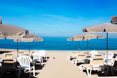 Chairs and umbrellas arranged on a beach by the ocean under a clear blue sky.