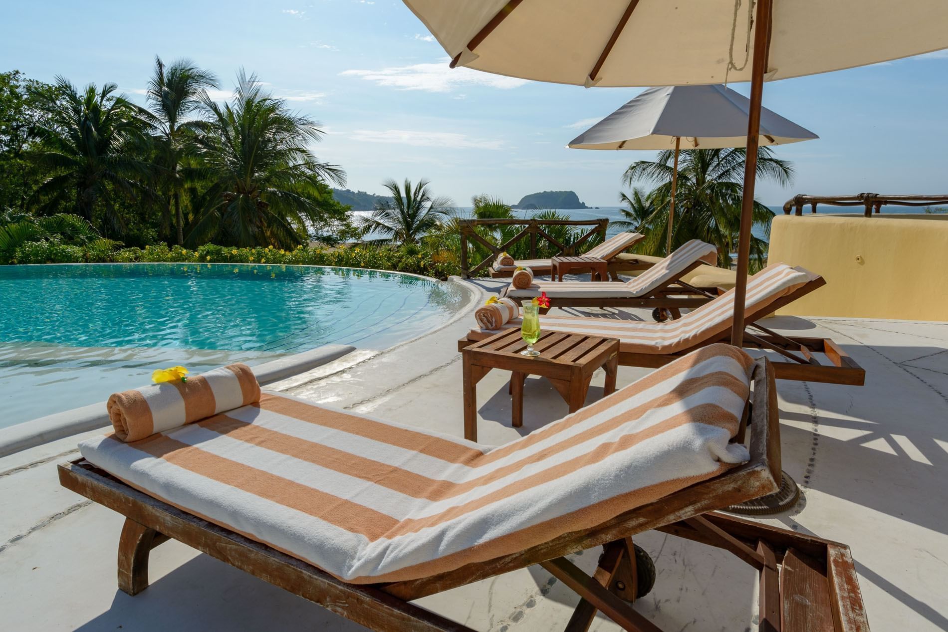 Pool area Lounge chairs with white umbrellas surrounding palm trees at Quinta Real Huatulco