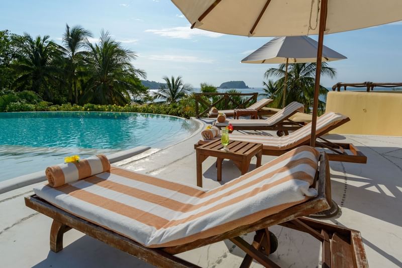 Pool area Lounge chairs with white umbrellas surrounding palm trees at Quinta Real Huatulco