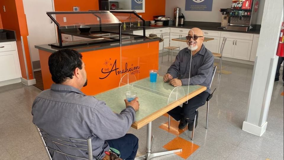 2 people at a table separated with a shield, The Anaheim Hotel