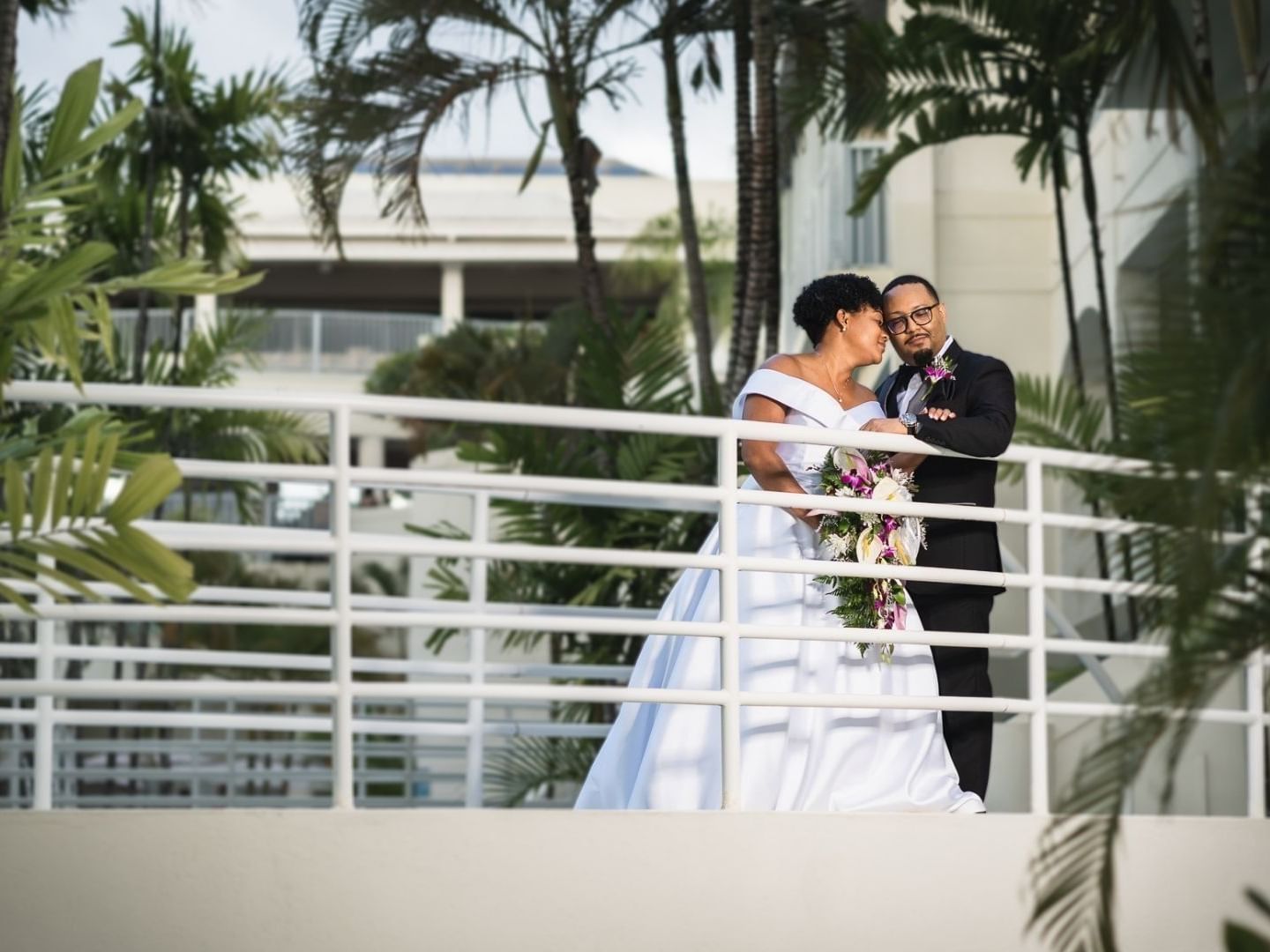 Newlyweds on a balcony surrounded by lush palm trees at Savannah Beach Hotel.