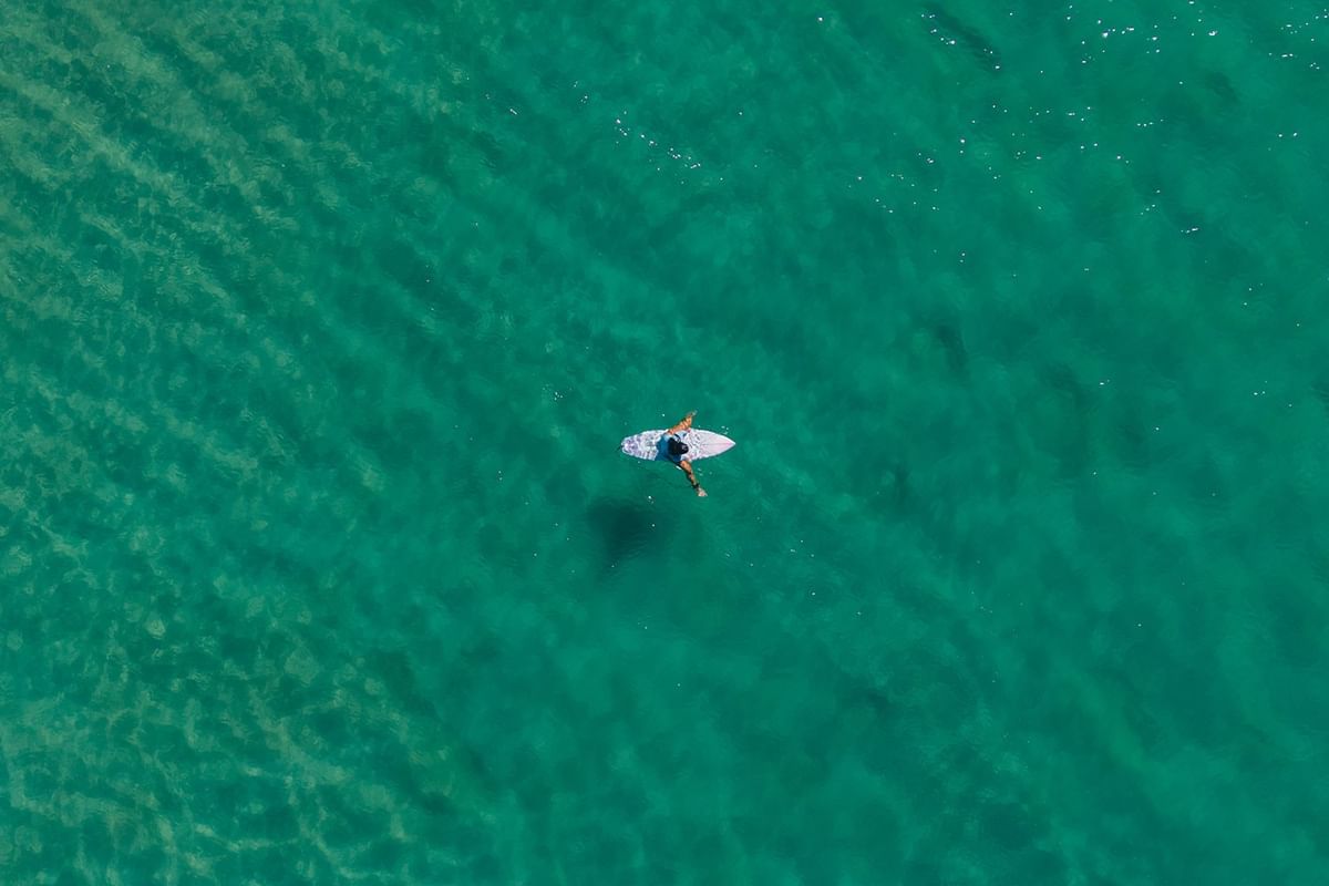 Turquoise ocean at Elysium Hotels displaying an aerial top-down view of a surfer paddling on surfboard in clear water