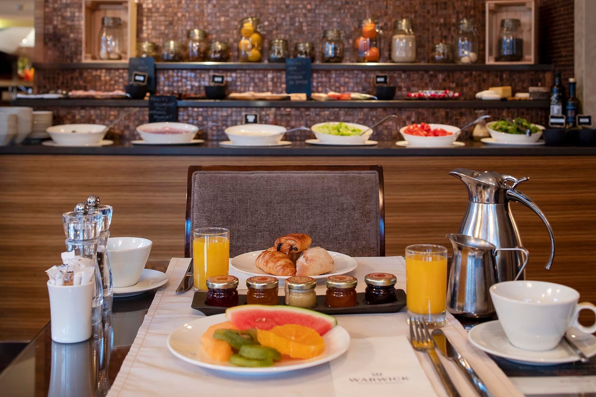 Well-set breakfast table featuring fresh fruit, croissants, & orange juice with a buffet in background at Téséo Restaurant