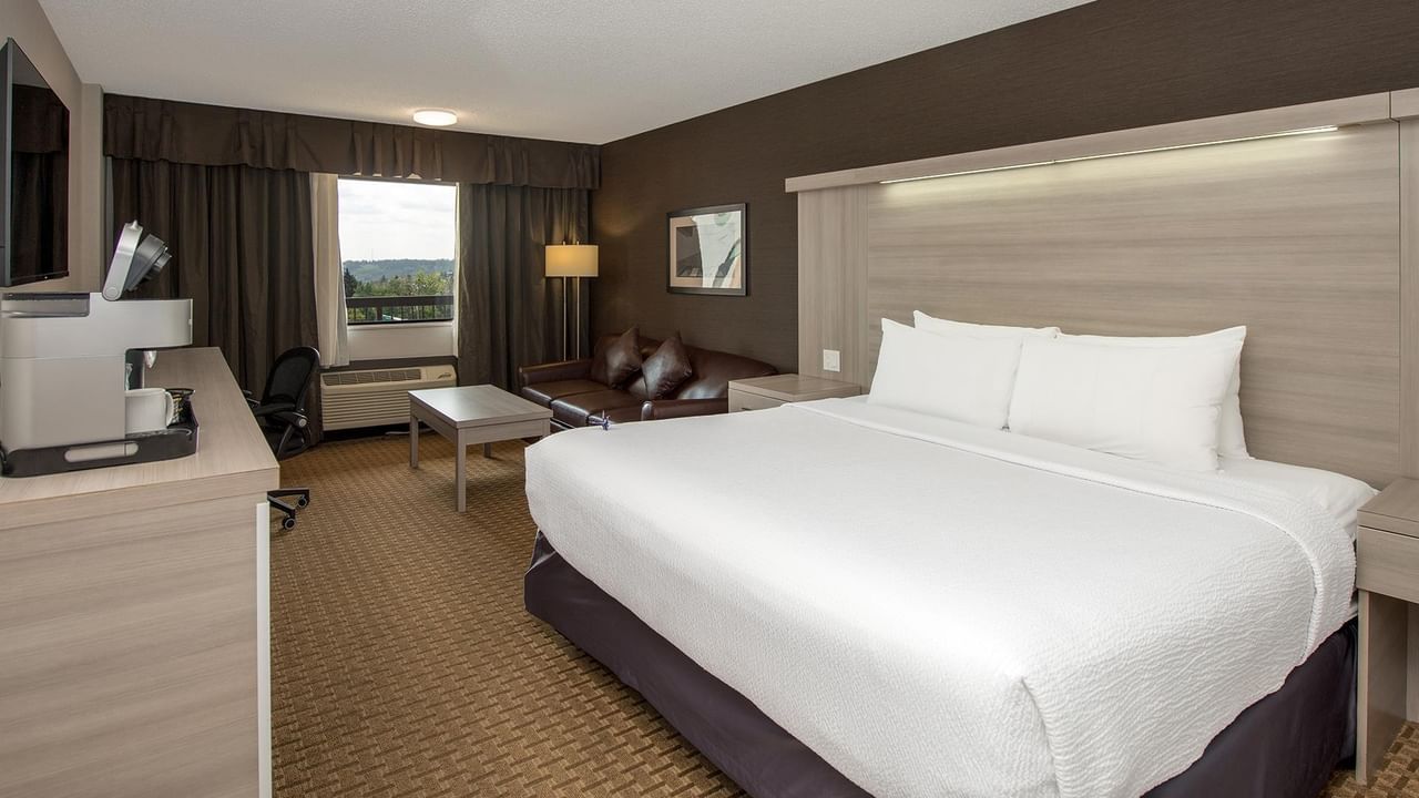 Modern hotel room with king bed, seating area, work desk, and window view at Coast Calgary University Area Hotel by APA