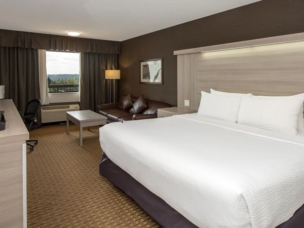 Coast Premium King room with white bedding, seating area, and mountain views at Coast Calgary University Area Hotel by APA
