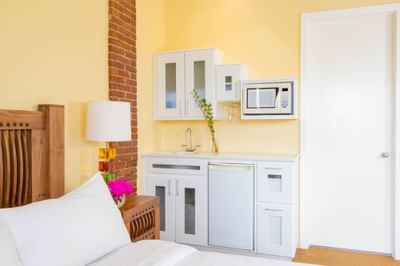 Bed-facing kitchenette with white pantry, appliances & exposed brick wall in Queen Premiere Mellow in Retro Suites