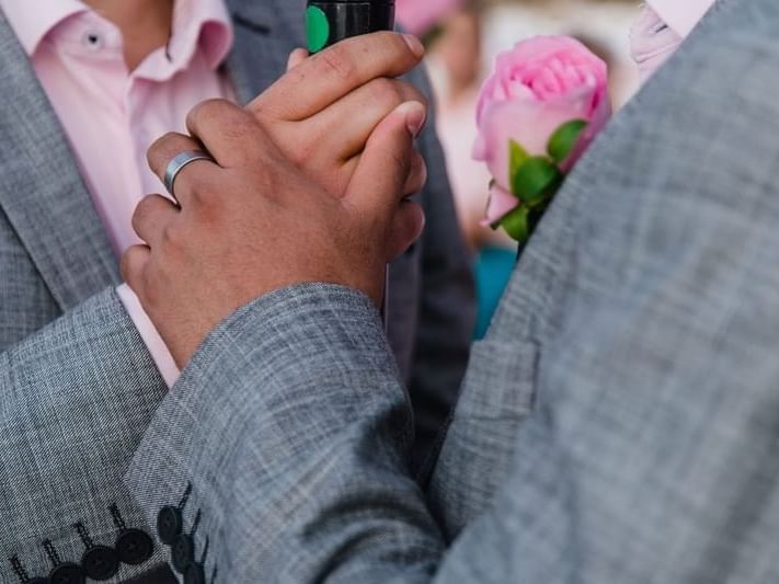 Two men in gray suits holding hands tenderly at a wedding at Fiesta Americana Travelty