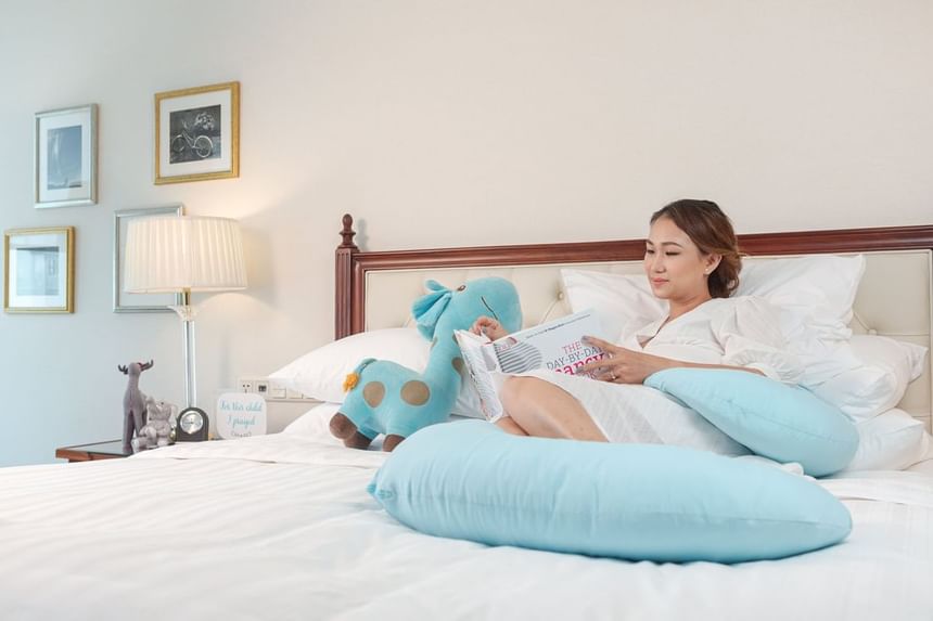 Pregnant mother laying on a bed with stuffed toys while reading a book at Park Hyatt Saigon