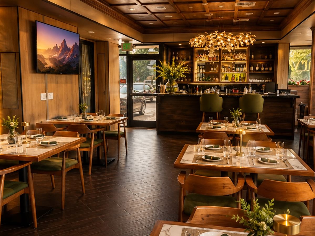 Arya restaurant interior with wooden tables, green accents, and warm lighting at Coast Burbank Hotel in Burbank
