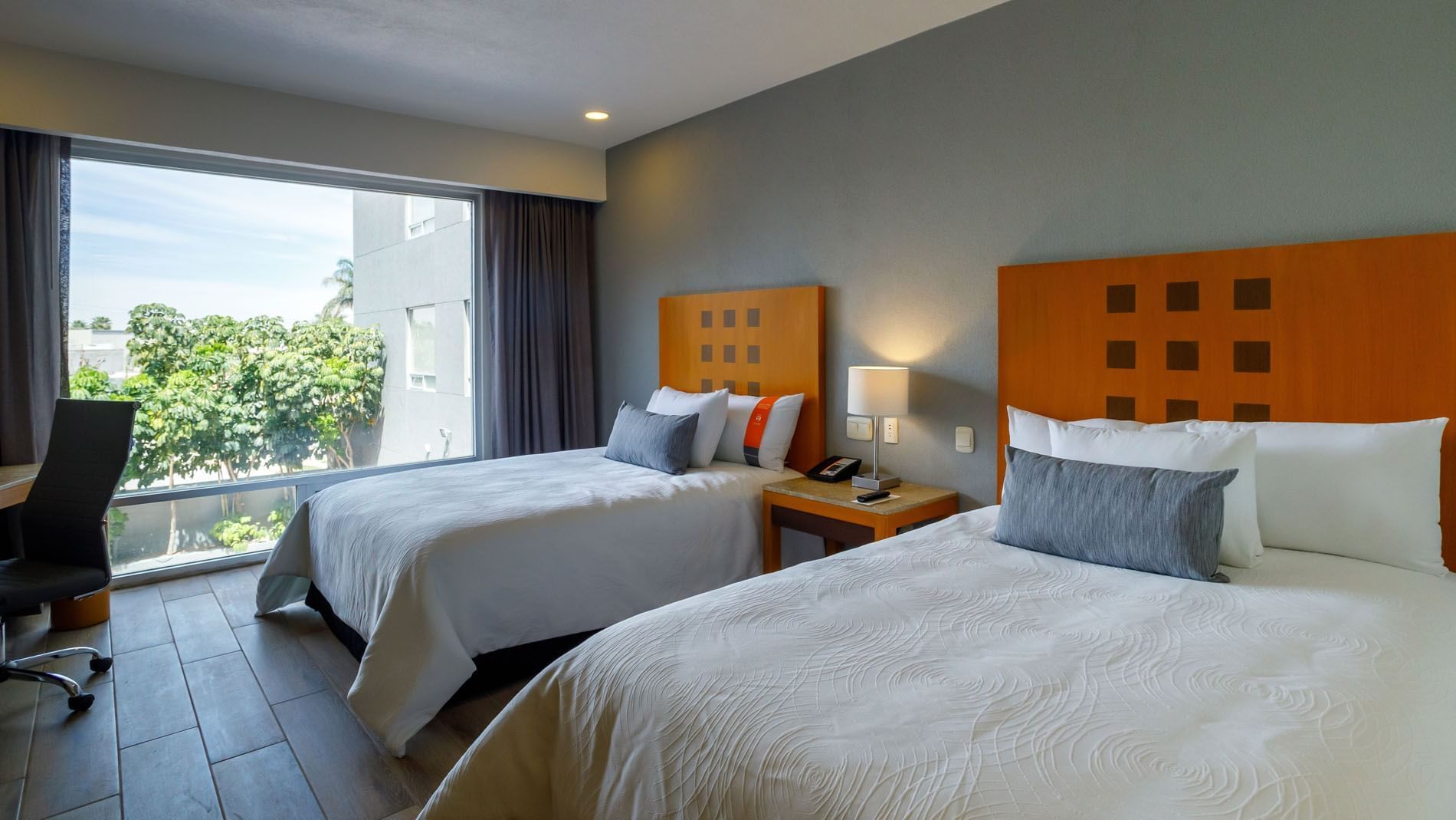 2 Double Deluxe room with two beds, wooden headboards, and a large window showing greenery at Real Inn Torreon