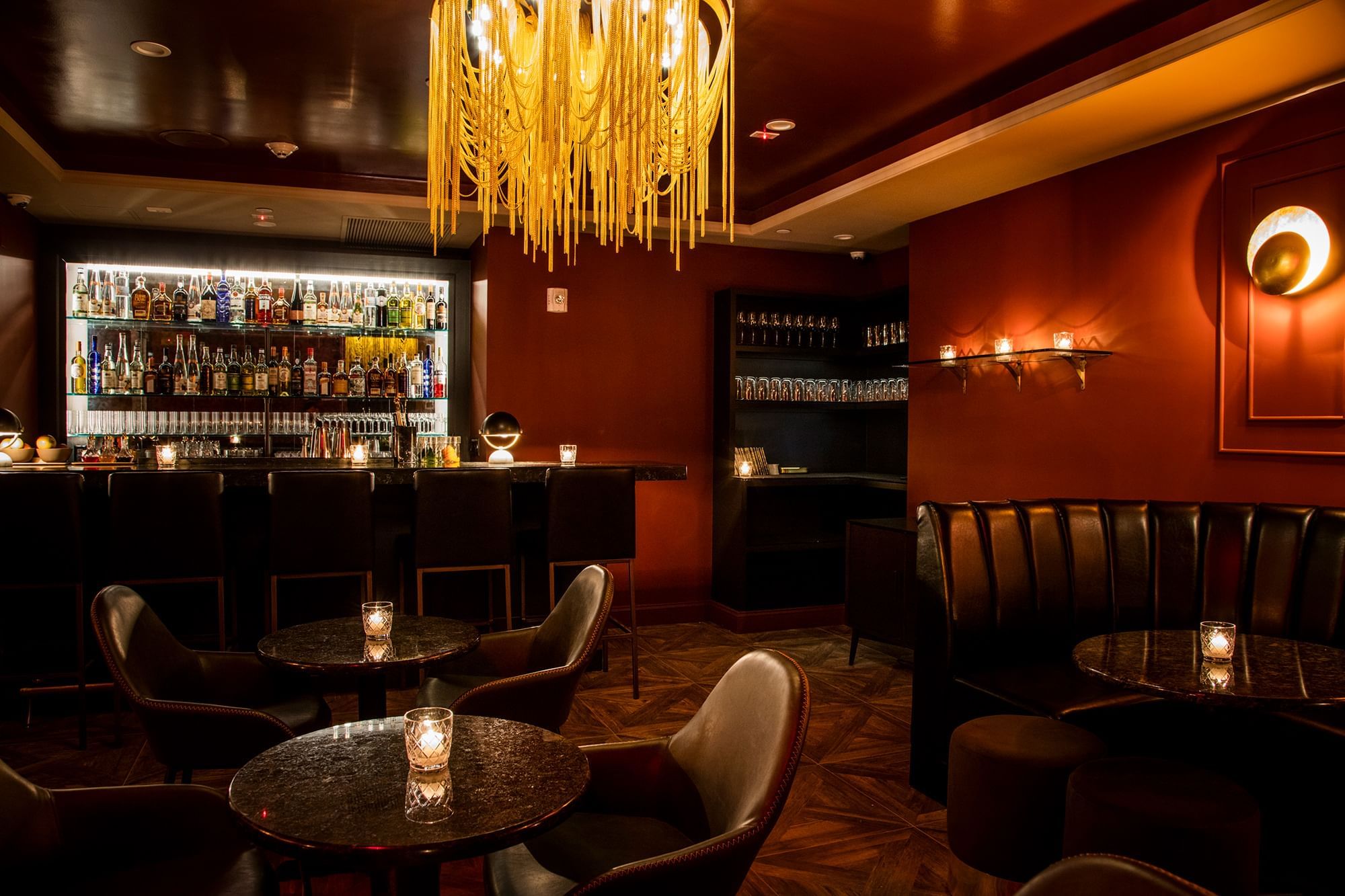 A dimly lit bar with a chandelier, leather booths, and tables with candles.