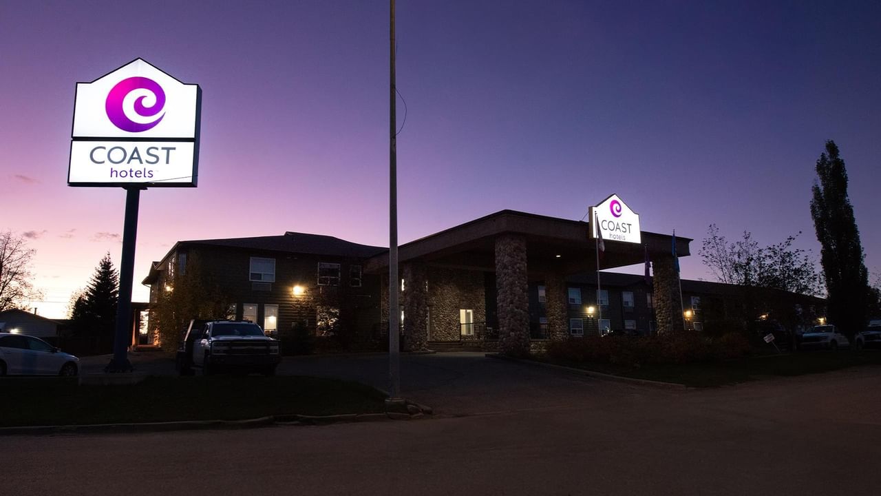 Coast Edson Hotel exterior at dusk with illuminated signage and stone facade against a purple and blue twilight sky.