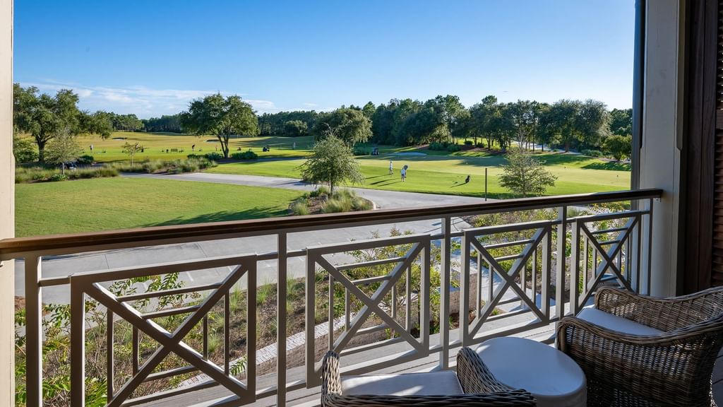 A balcony with wicker chairs and a table overlooking a golf course and trees.
