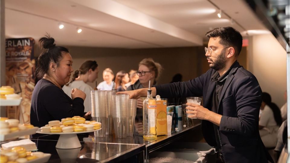 Bartender preparing refreshments beside trays of macarons and stacked cups during a wellness event at Hotel X Toronto