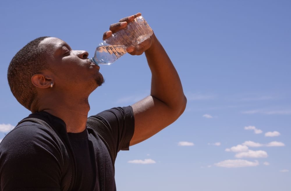 A man drinks a bottle of water against a clear blue sky.