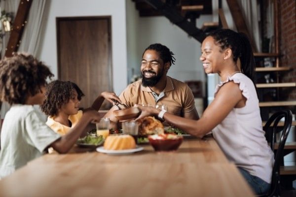 A family with two young kids sits around a table sharing food and smiling during family dinner.