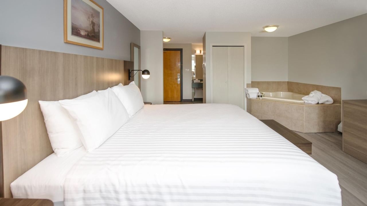 Hotel room with a large bed, white bedding, and a bathtub in the corner.