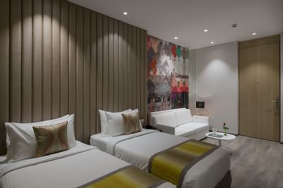 Twin beds by a sofa in Studio Twin Room at Eastin Residences Vadodara