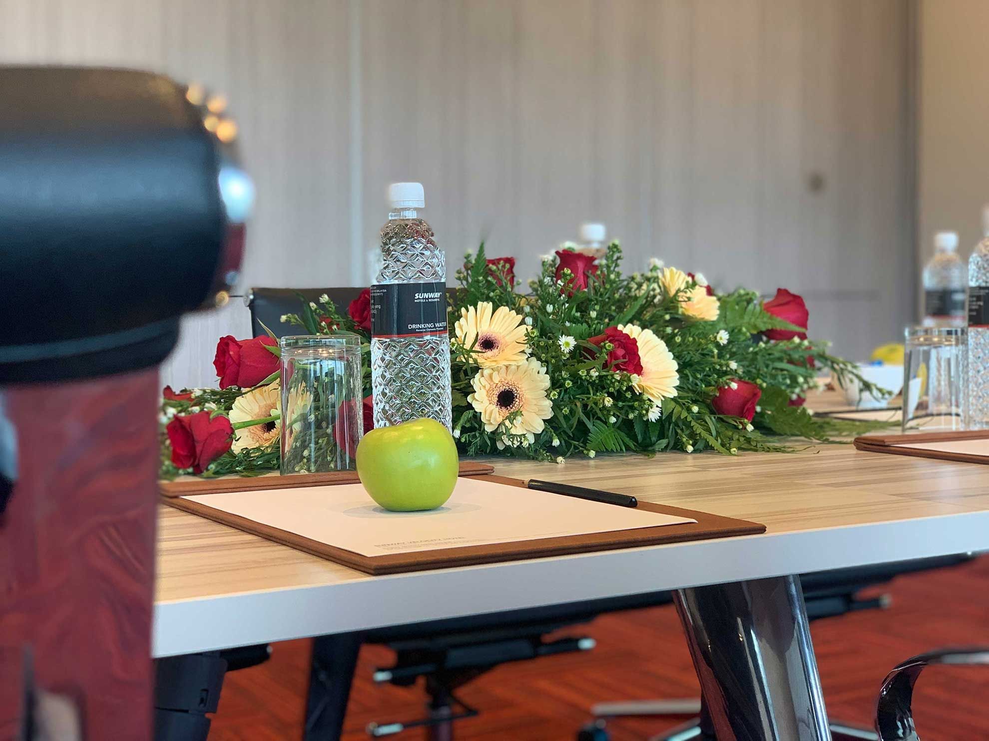 A conference table with flowers, water bottles, a green apple, and notepads in a meeting room at Sunway Velocity Hotel