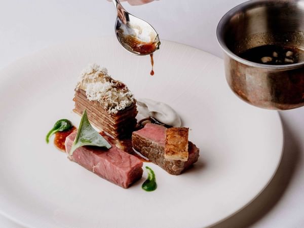 Chef adds sauce to a dish with meat and vegetables at The Capital Hotel, Apartments & Townhouse - London.