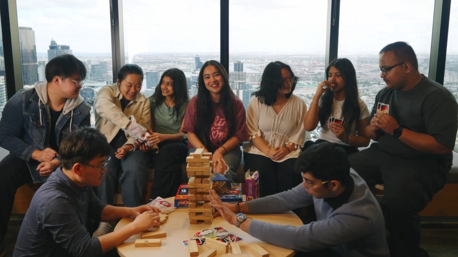 Group of students sitting around a table playing a game with cards and wooden blocks in a high-rise building.