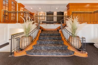 Grand central staircase with a black patterned carpet, flanked by two large plant vases at The Boulevard Inn & Bistro