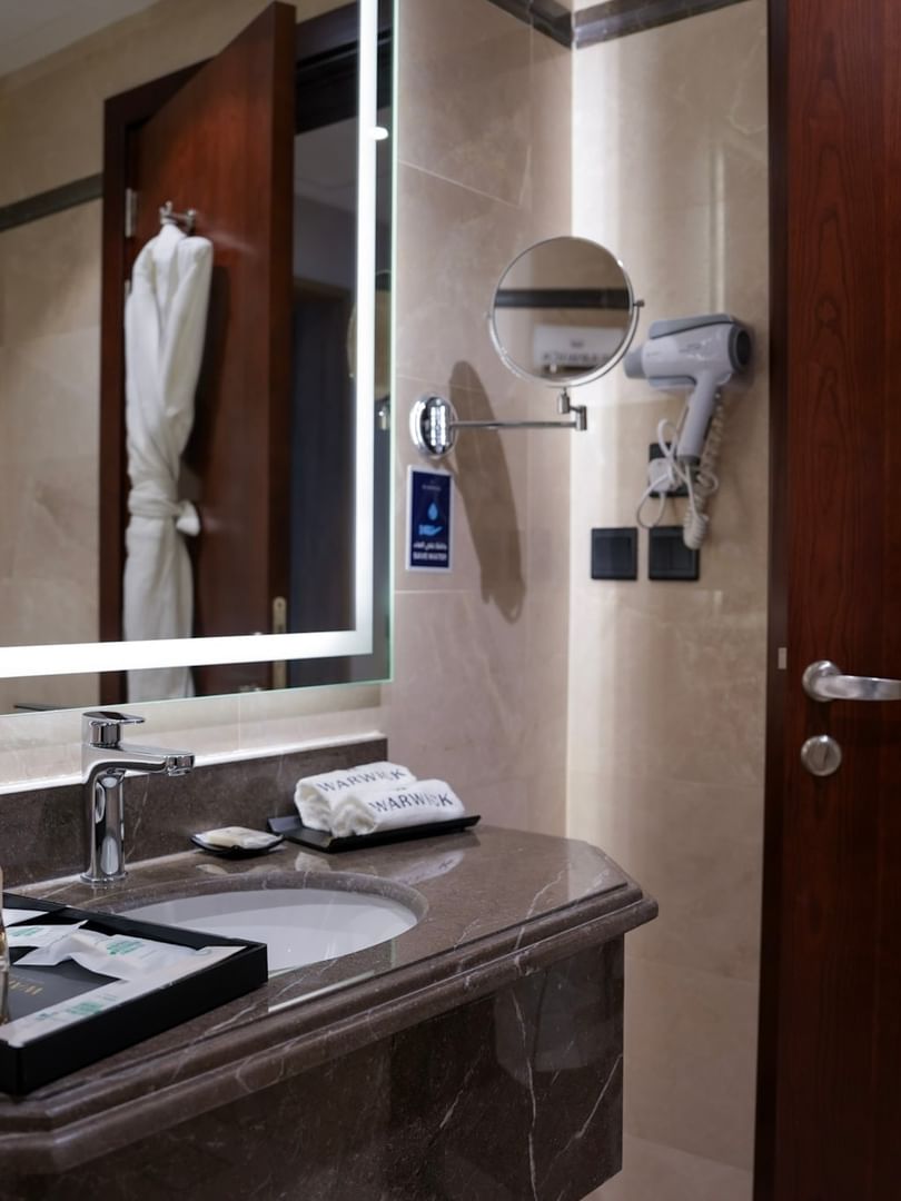 Elegant bathroom with a marble sink and white bathrobe at Warwick Hotel & Spa Jeddah.