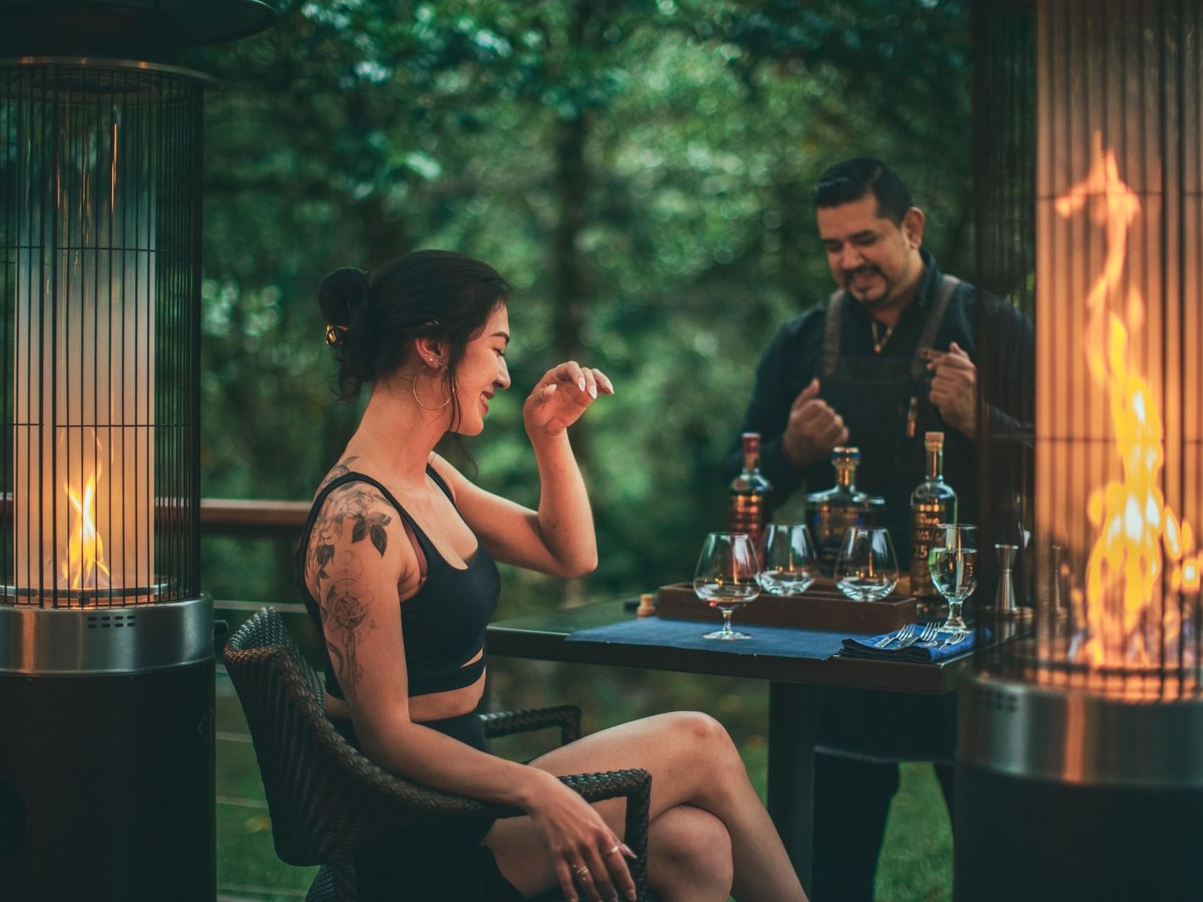 Woman sitting by a table with drinks, outdoor patio heater nearby at El Silencio Lodge and Spa