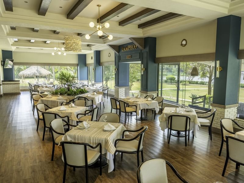 Restaurante with white dining tables, chairs and large windows with garden view at Fiesta Inn Tampico