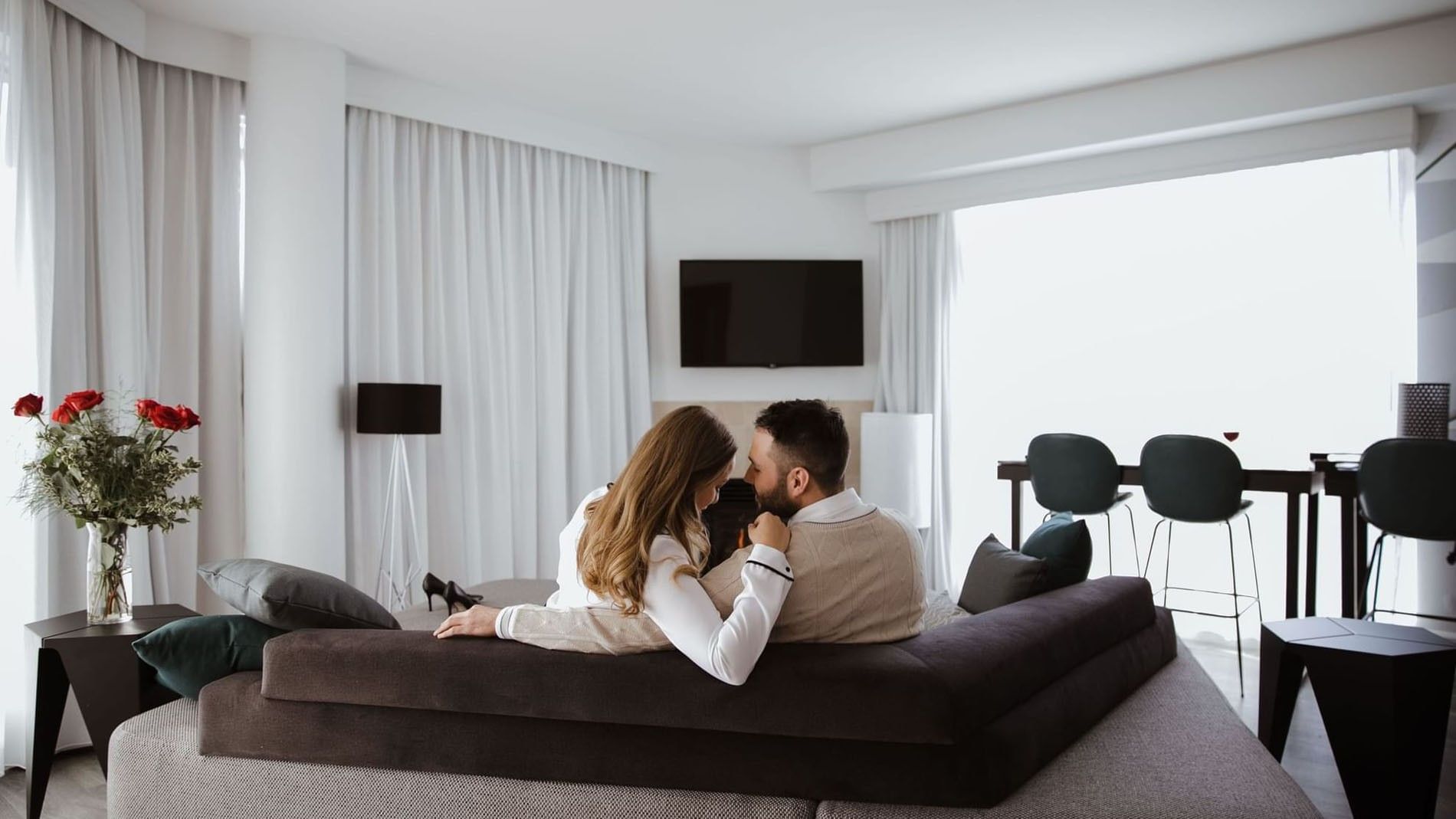 Couple on a grey sofa by a fireplace and TV in a luxury suite at Warwick Le Crystal Montreal