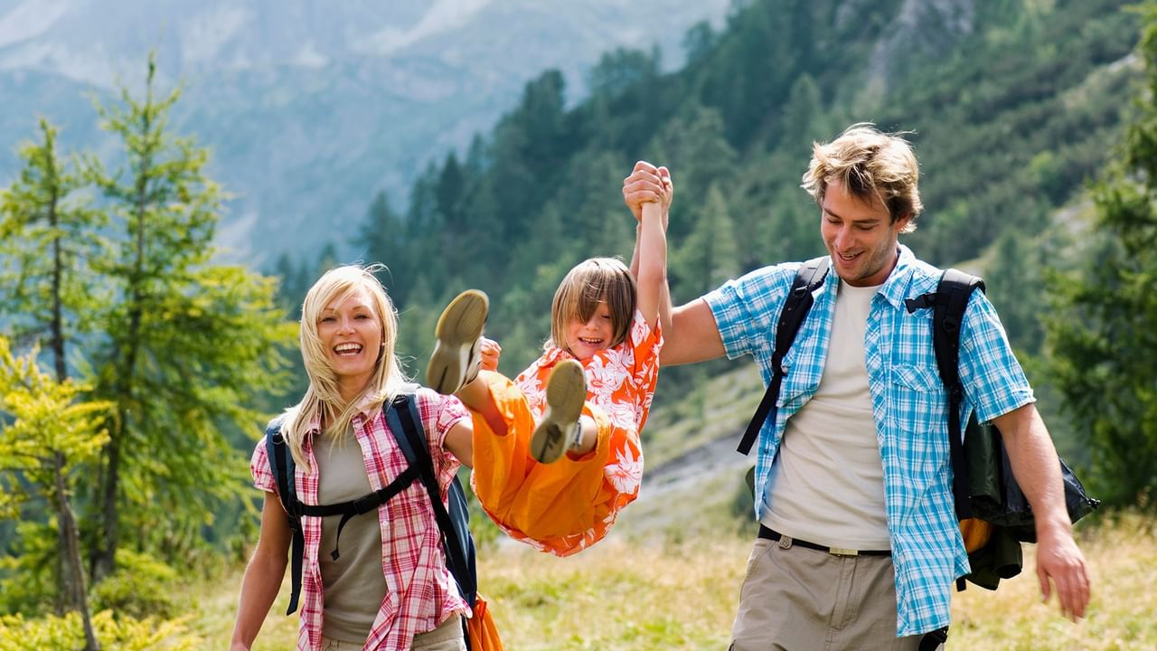 Family hiking together on a mountain trail with forested peaks during summer