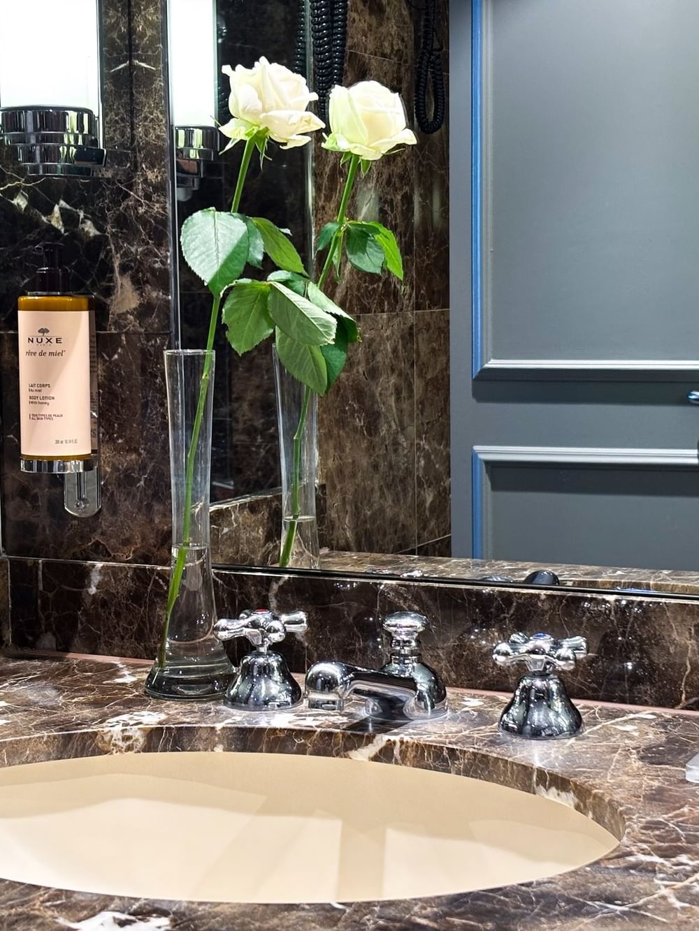 Junior Suite Privilege View bathroom featuring sink with roses in vases by wall mirrors at Warwick Grand Place Brussels
