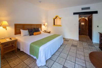 Cozy hotel room with bed, nightstands, lamps, wooden door, and tiled floors.