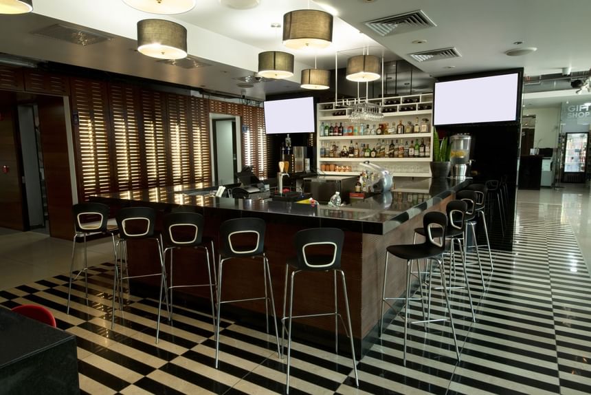 Bar with black stools, countertop, and a well-stocked shelf of liquor at D Sabana Hotel