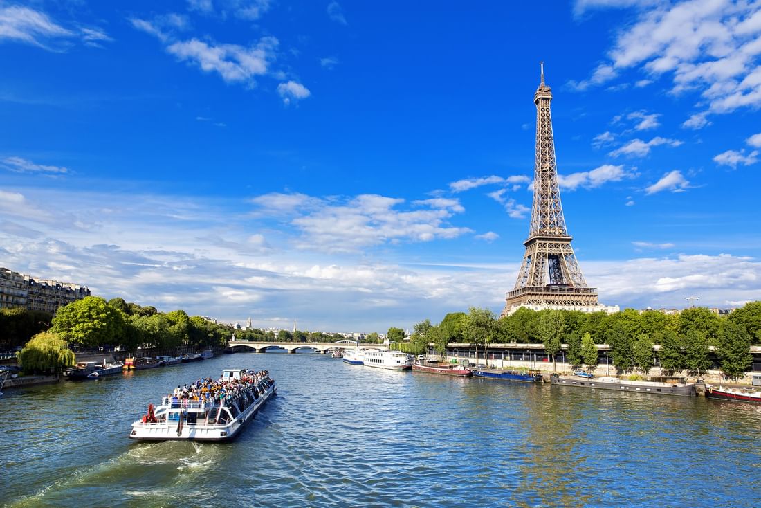 River boat by the Eiffel Tower under a blue sky with clouds near the Warwick Paris Champs Elysées
