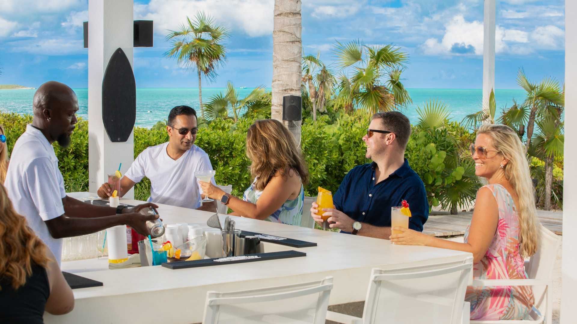 Guests enjoying drinks with H2O staff at the bar overlooking Long Bay Beach, H2O life.style.resort., Turks and Caicos