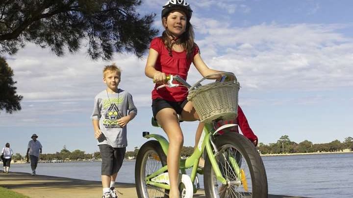 Two happy children cycling on a sunny day near the Sebel Mandurah boardwalk by the water