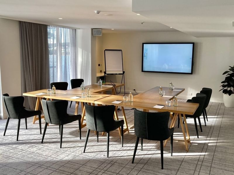 The Pacific Room at Elysium Manly with a U-shaped wooden table and black chairs near an interactive screen