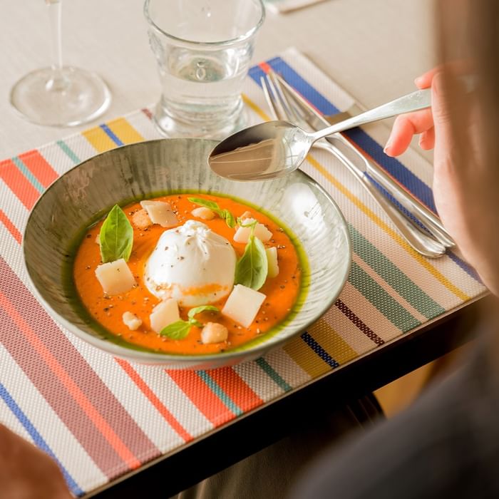 Una persona mangia una zuppa con un cucchiaio su un tavolo colorato di Falkensteiner Hotel & Spa Jesolo
