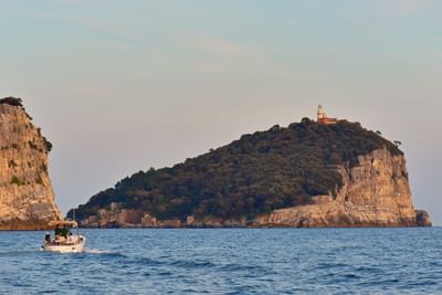 Small boat cruising past dramatic coastal cliffs and lighthouse-topped island at Grand Hotel Portovenere