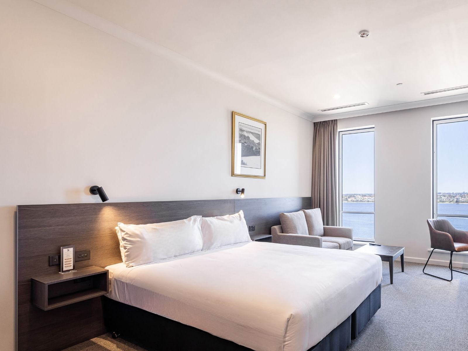 Deluxe King River View featuring a king-size bed, armchair, and large windows with sheer curtains at Duxton Hotel Perth