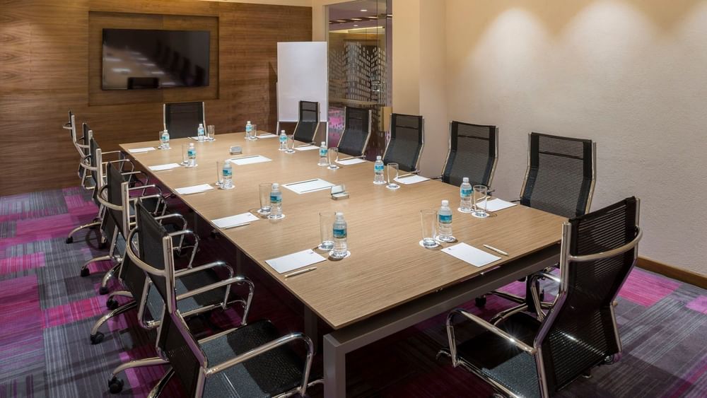 Modern boardroom with a light wood table, black mesh chairs, and bottled water at Camino Real Pedregal Mexico