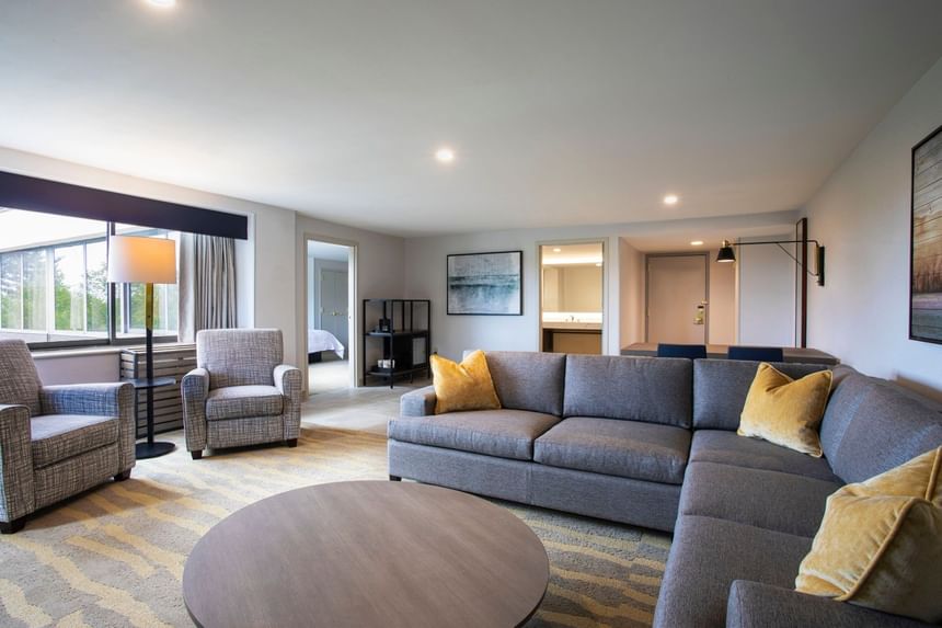 Spacious suite living area with sectional couch and coffee table near a window at Sable Oaks Weddings and Events