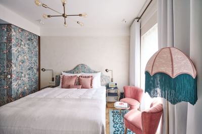Chic room featuring a floral wallpaper accent, a bed with pink pillows, and plush seating by the window at Hotel Motto Vienna