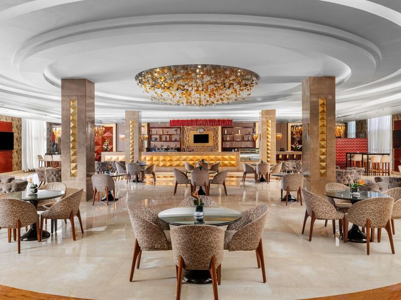 غرفة طعام أنيقة مع طاولات وكراسٍ دائرية، ثريا كبيرة، وديكورات فاخرة.