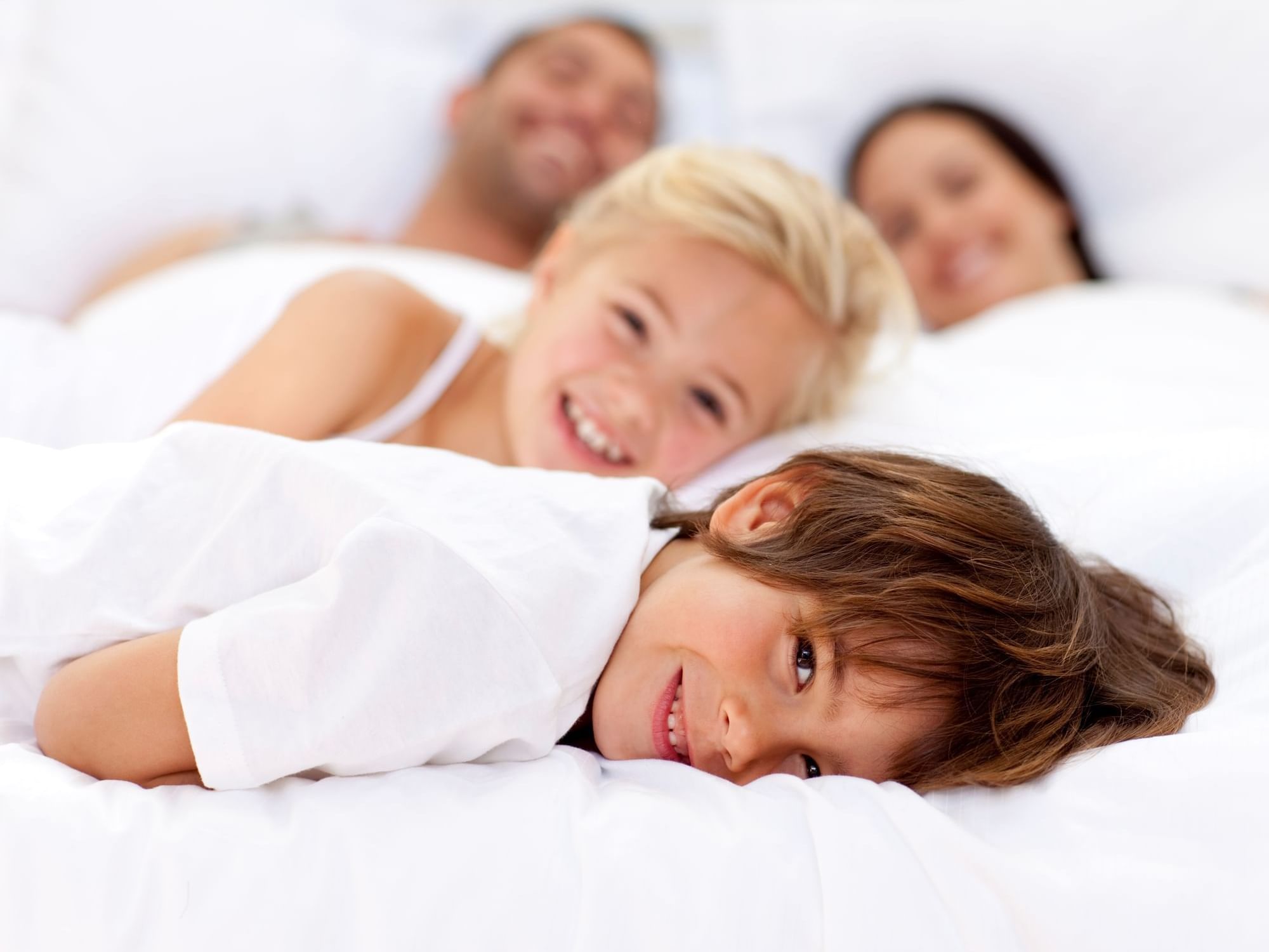 Happy kids lying in bed by their parents in a room at Hotel Grand Chancellor Townsville