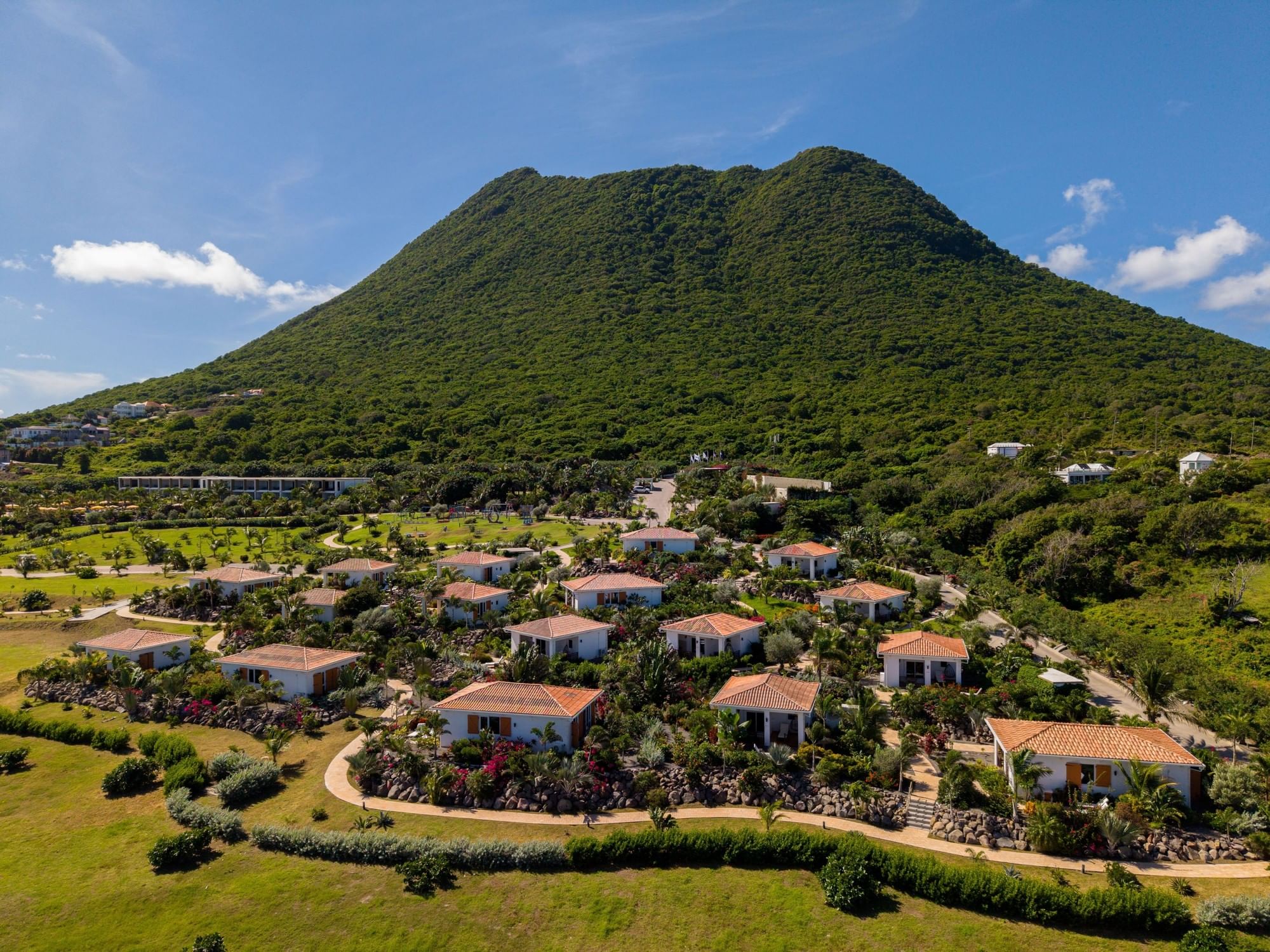 Aerial view with colorful resort villas nestled beneath a massive lush green mountain peak at Golden Rock Resort